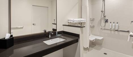 Un baño moderno con lavamanos de encimera negro, un espejo grande, ducha con cabezal de ducha manual y un perchero.
