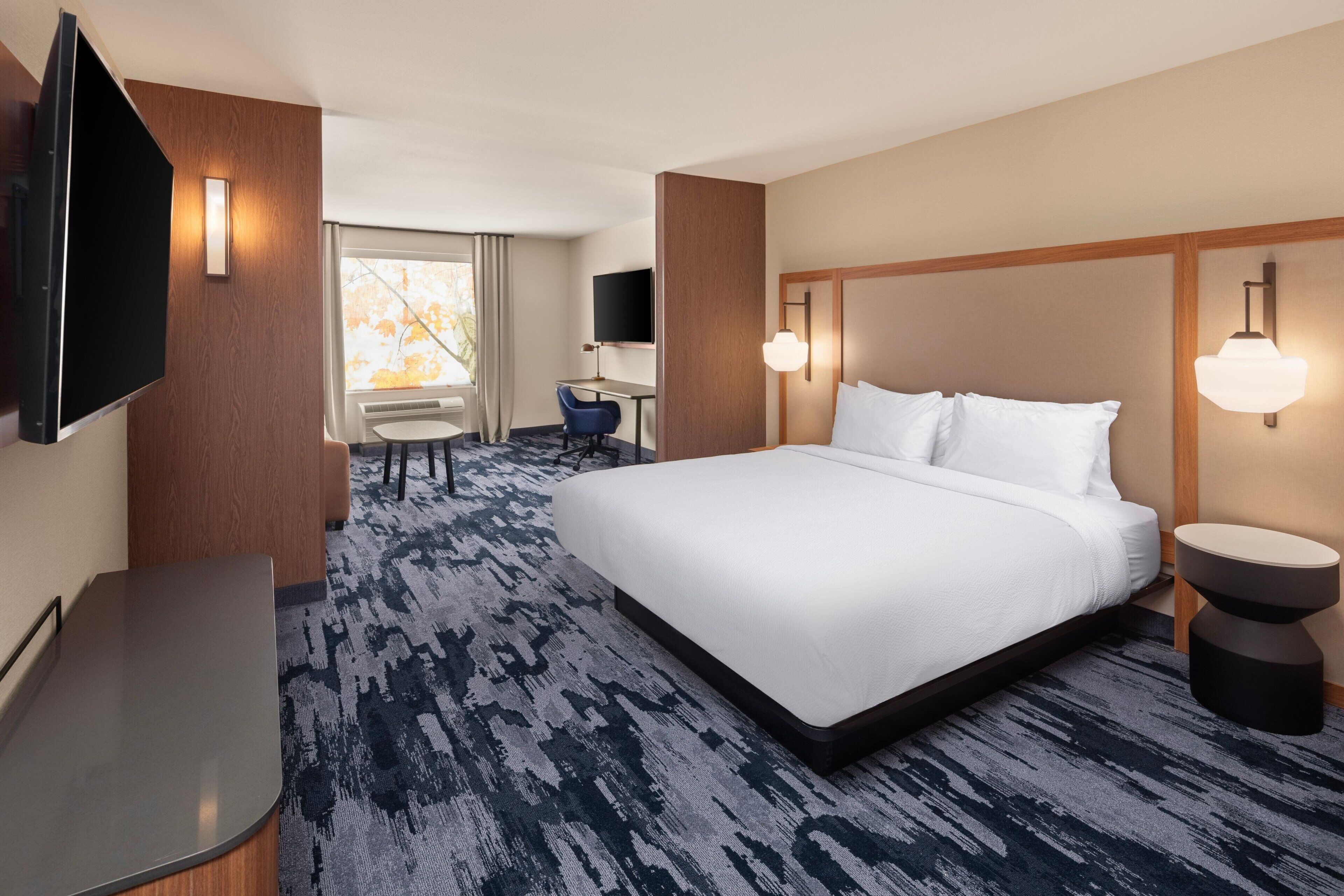 Habitación de hotel con una cama grande, un escritorio, una silla, un televisor y una ventana con cortinas.