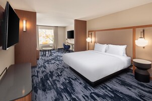 Habitación de hotel con una cama grande, un escritorio, una silla, un televisor y una ventana con cortinas.