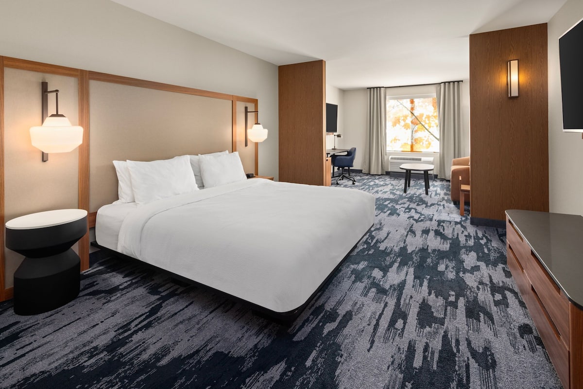 A hotel room with a large bed, a desk, a chair, a TV, and a window with curtains.