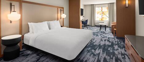 A hotel room with a large bed, a desk, a chair, a TV, and a window with curtains.
