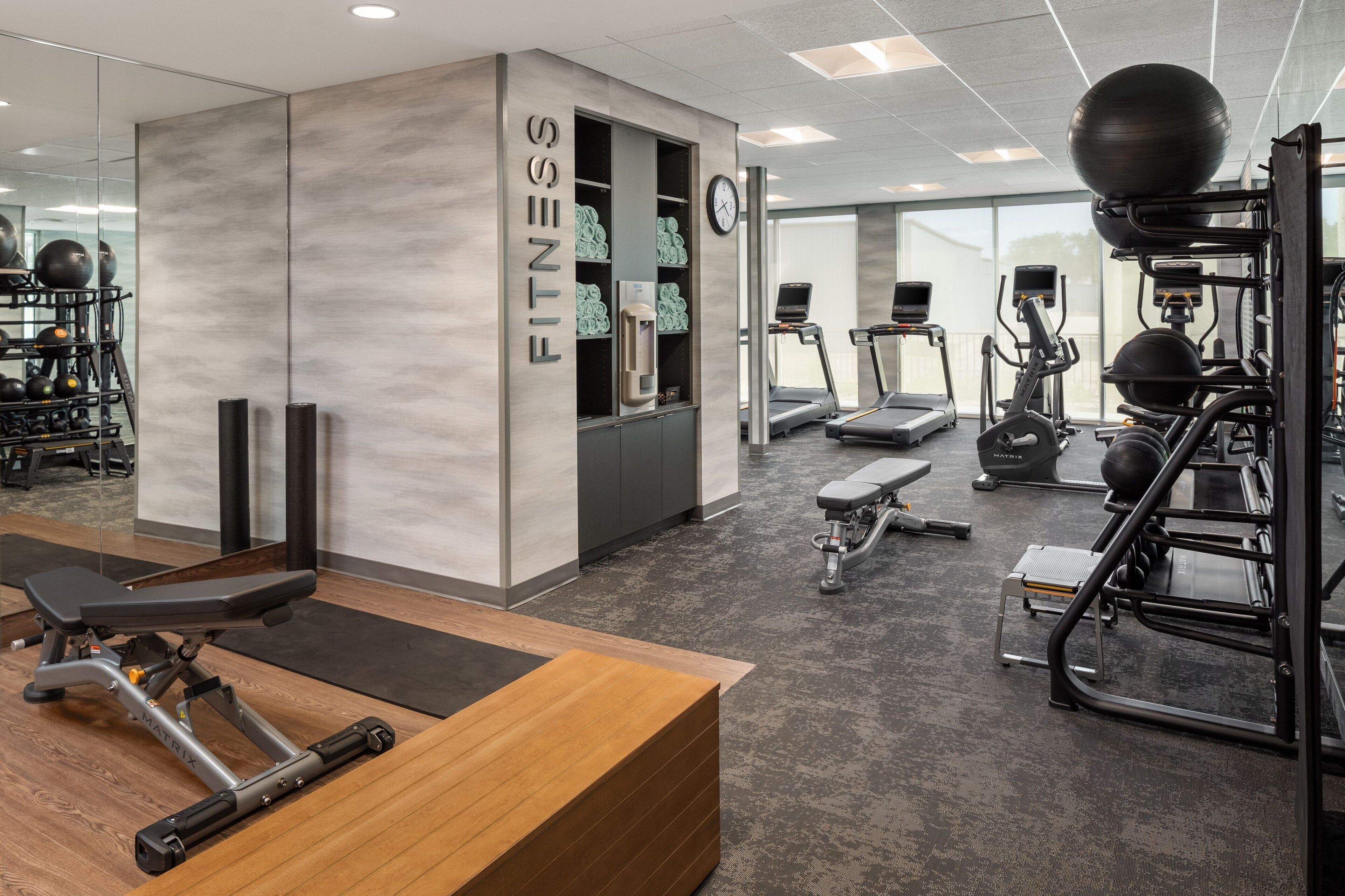 Une salle de sport moderne équipée de machines de cardio, d’appareils de musculation et dotée d’un comptoir d’accueil en bois.