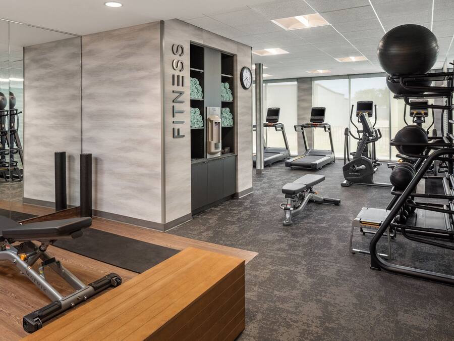 Une salle de sport moderne équipée de machines de cardio, d’appareils de musculation et dotée d’un comptoir d’accueil en bois.