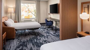 A hotel room with a bed, a desk, a chair, a TV, and a window with curtains.