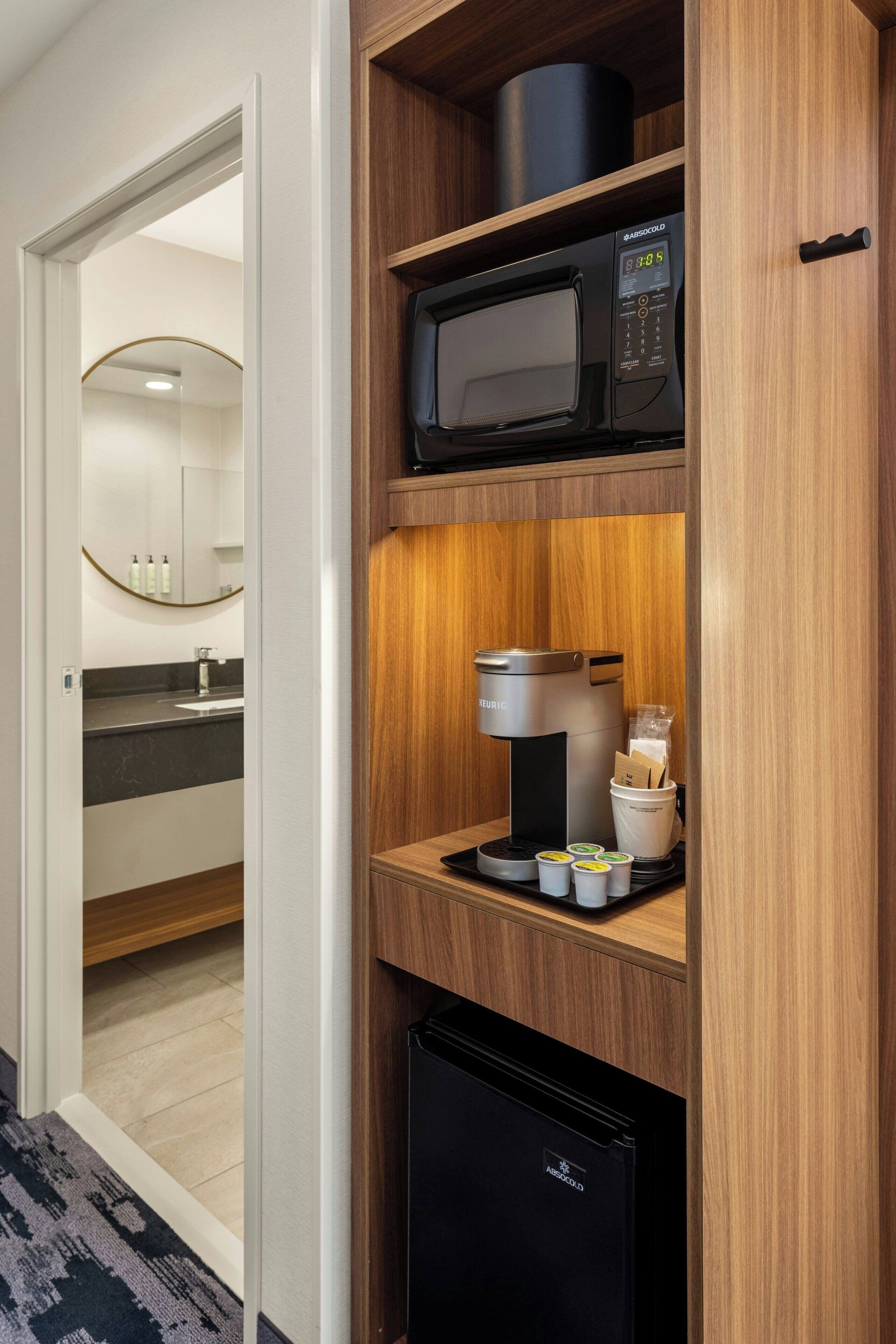 Una kitchenette compacta con cafetera, microondas y refrigerador.
