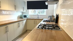 A modern kitchen with light-colored cabinets, a wooden countertop, a gas stove, and a microwave. - Vibrant 6 bed Stylish Home in Heart of Southsea (Portsmouth)