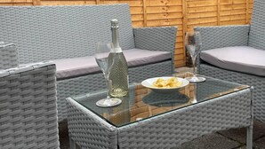 A wicker sofa set with cushions, a glass table, a bottle of champagne, and a plate of chips. - Vibrant 6 bed Stylish Home in Heart of Southsea (Portsmouth)