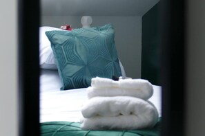A hotel room with a bed, a green patterned pillow, and neatly folded white towels. - Vibrant 6 bed Stylish Home in Heart of Southsea (Portsmouth)