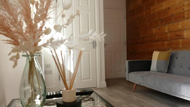 A living room with a glass coffee table, a vase with dried flowers, a grey sofa, and a wooden wall. - Vibrant 6 bed Stylish Home in Heart of Southsea (Portsmouth)