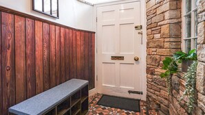 A hallway with a white door, wooden paneling, a bench, and a stone wall with a window. - The Old Bulls Head (High Peak)