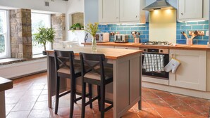 A kitchen with a central island, white cabinets, blue backsplash, and a stone wall. - The Old Bulls Head (High Peak)