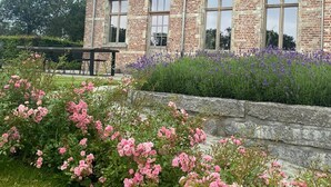 A two-story brick house with a stone retaining wall and a garden with pink roses.