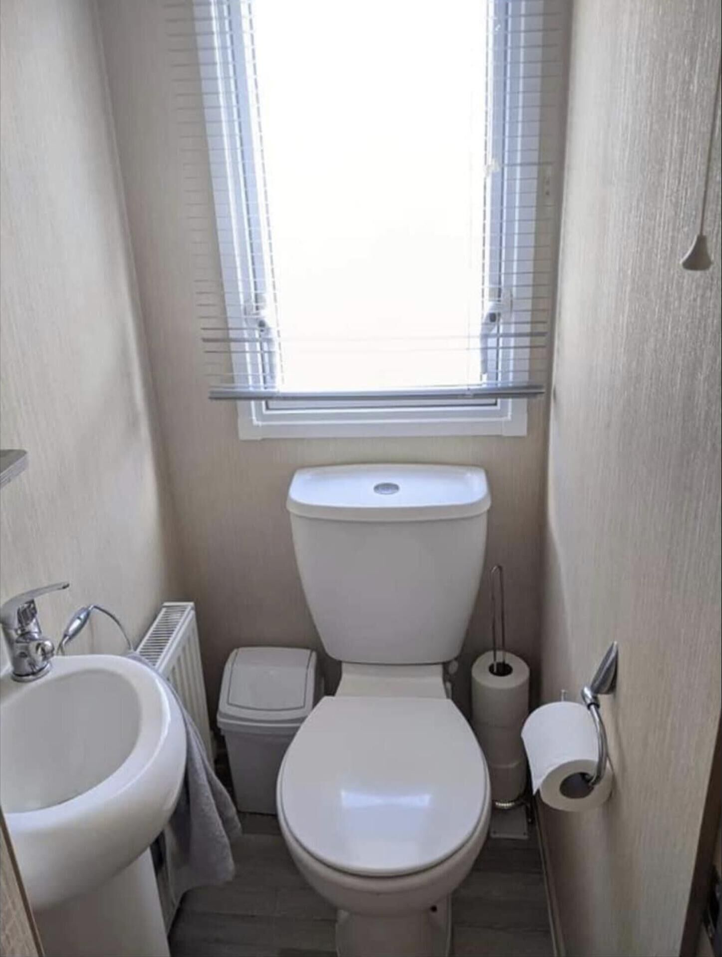 Une petite salle de bain compacte, équipée de toilettes, d’un lavabo et d’une fenêtre.