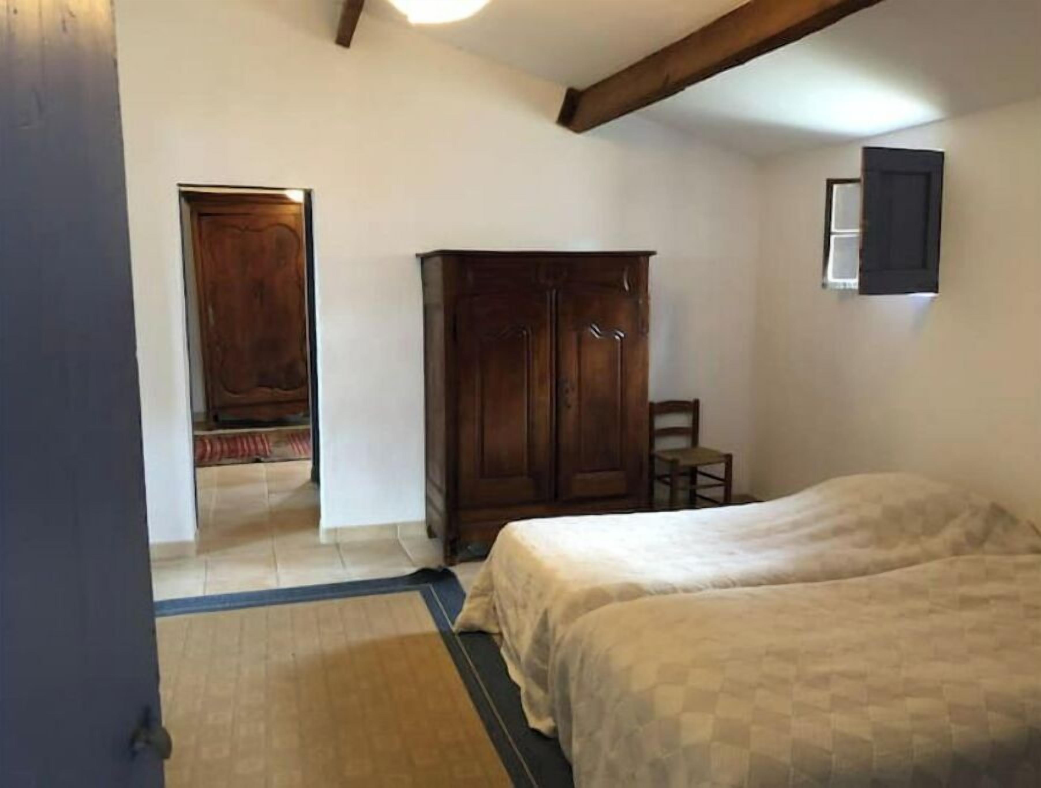 A room with two beds, a wooden wardrobe, a chair, and a small window.