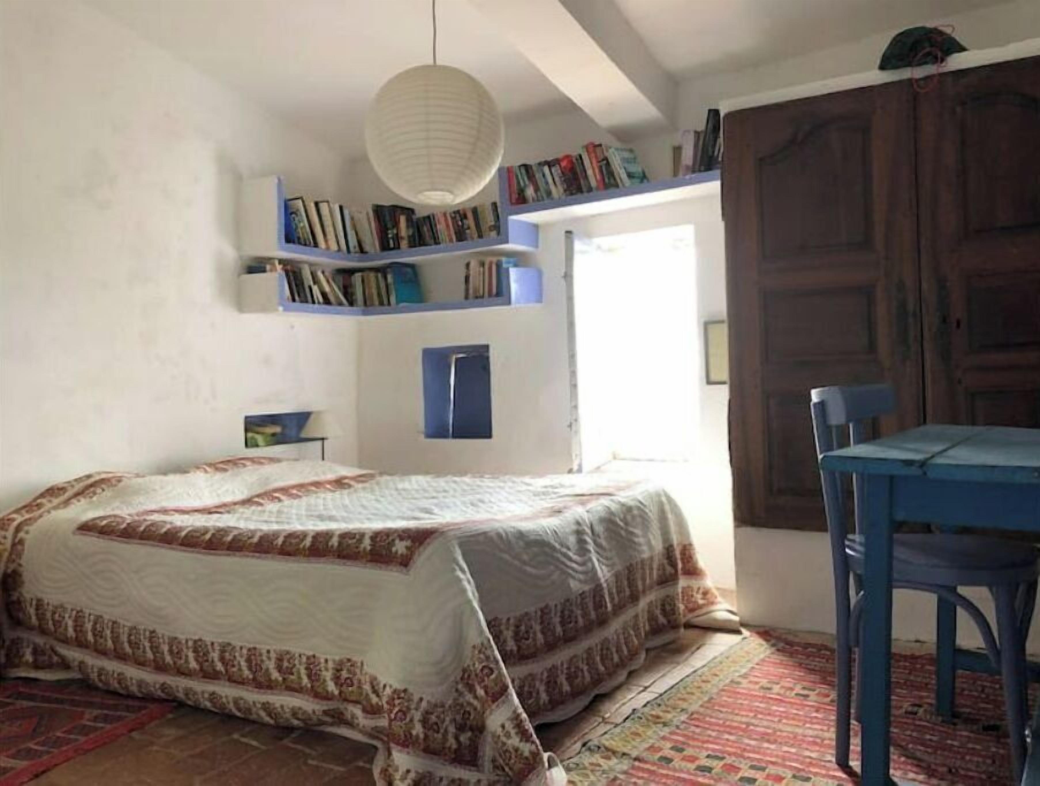 A bedroom with a bed, a chair, a bookshelf, and a door.