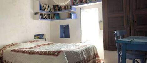 A bedroom with a bed, a chair, a bookshelf, and a door.