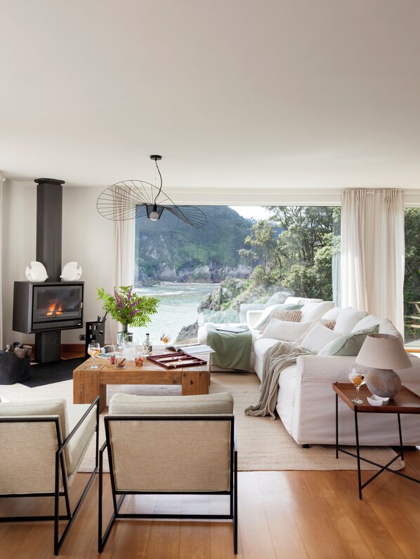 A modern living room with a fireplace, comfortable seating, a coffee table, and a view of the ocean. - Wishome — A dream villa by the sea for a fall getaway. Heated pool (Pechón)