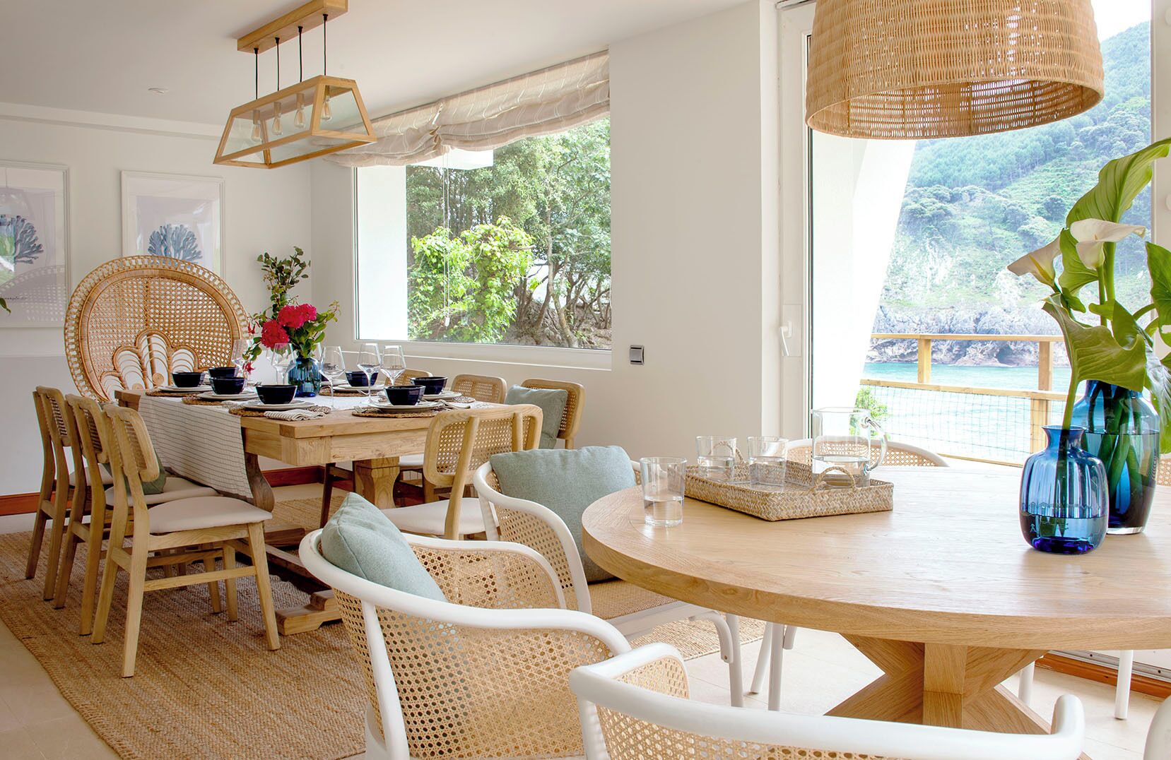A dining area with a round wooden table, wicker chairs, and a view of a mountainous landscape through large windows.