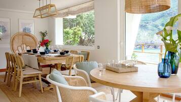 A dining area with a round wooden table, wicker chairs, and a view of a mountainous landscape through large windows.