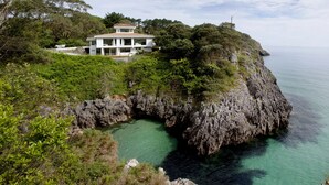 Ein Küstenanwesen mit einem zweistöckigen Haus mit Blick auf eine felsige Klippe und türkisblaues Wasser.
