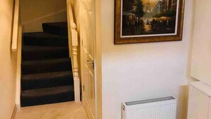 A hallway with a staircase, a radiator, and a framed picture on the wall. - 3-bed House in Armagh City (Armagh)
