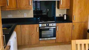 A kitchen with wooden cabinets, a stove, an oven, and a hanging light fixture. - 3-bed House in Armagh City (Armagh)