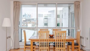 A dining area with a table and chairs, a lamp, and a view of the city through large windows.