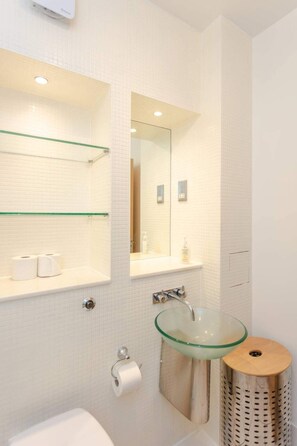 A modern bathroom with a glass sink, white tiled walls, and a mirror above the sink.
