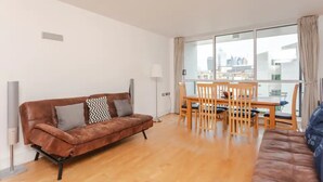 A modern living room with a brown leather sofa, a dining table with chairs, and large windows with curtains.