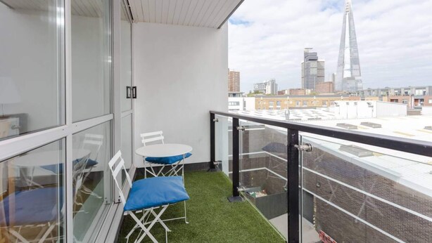 A balcony with a glass railing, a small table with chairs, and a view of a cityscape including a tall building.