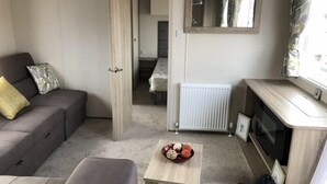 Ein kompakter Wohnbereich mit einer Couch, einem kleinen Tisch mit Dekoration, einem Heizkörper und einem Fernseher auf einem Holzständer.