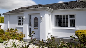 A white two-story house with a tiled roof, a front door with a glass panel, and a window with a grid pattern. - Charming 4-bed Cottage in Dungannon (Dungannon)