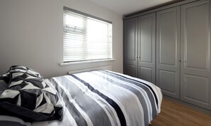 Une chambre à coucher avec un lit, une fenêtre avec des stores et une armoire.