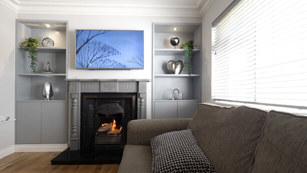 A living room with a fireplace, grey sofas, and decorative shelves. - Charming 4-bed Cottage in Dungannon (Dungannon)