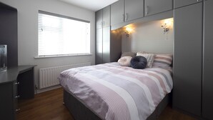 A bedroom with a bed, a dresser, a window with blinds, and a wall-mounted light fixture. - Charming 4-bed Cottage in Dungannon (Dungannon)