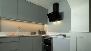 A modern kitchen with grey cabinets, a stainless steel sink, a built-in oven, and a black range hood. - Charming 4-bed Cottage in Dungannon (Dungannon)