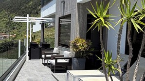Une terrasse extérieure moderne, dotée d’un espace salon, de plantes en pot et offrant une vue sur un paysage montagneux.