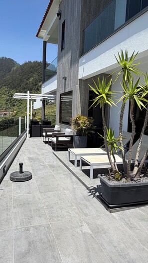 A modern outdoor patio with a seating area, potted plants, and a view of a mountainous landscape.