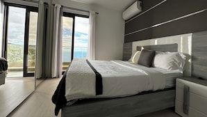 Une chambre moderne dotée d’un grand lit, d’une table de chevet, d’une armoire intégrée et offrant une vue sur la mer grâce à une porte-fenêtre coulissante.