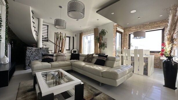 Un salon moderne avec un canapé d’angle, une table basse en verre et un coin repas comprenant une table haute et des chaises.