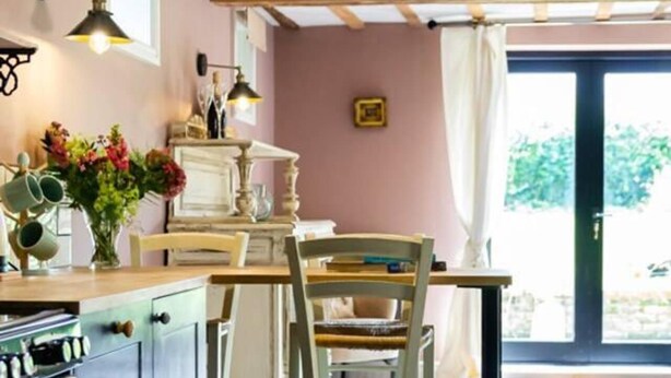 A kitchen with a wooden ceiling, a dining table with chairs, a stove, and a window with a view of greenery.