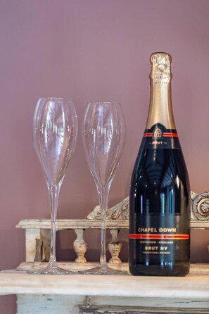 A bottle of 'Chapel Down' Brut NV champagne and two empty champagne flutes on a wooden surface with a decorative backdrop.