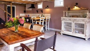 A rustic dining area with a wooden table and chairs, a white cabinet with a glass door, and a kitchen in the background.