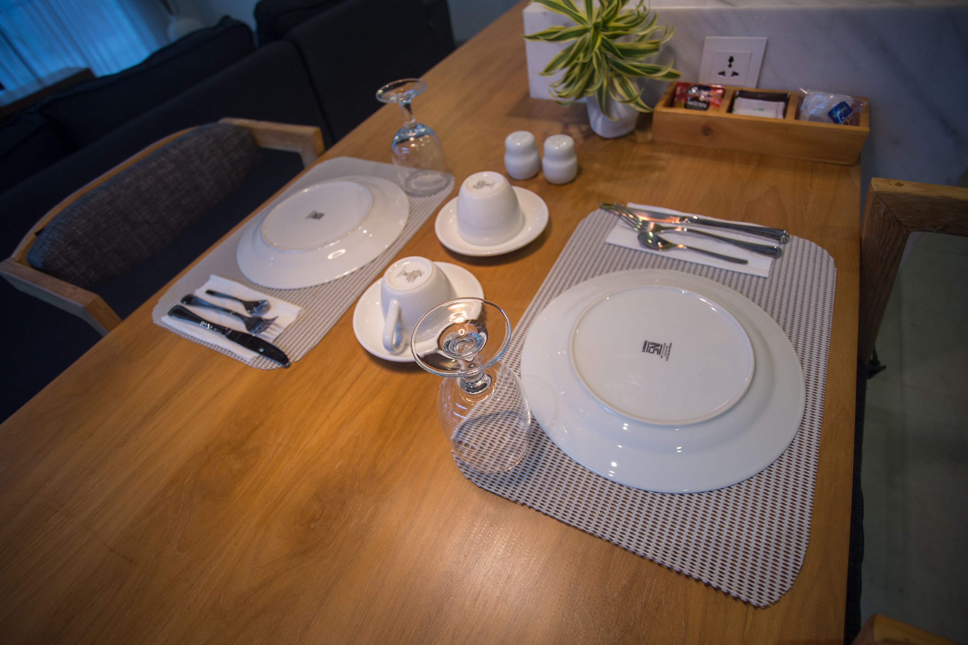 A dining table set with white plates, bowls, cutlery, and glasses, with a placemat and salt and pepper shakers.