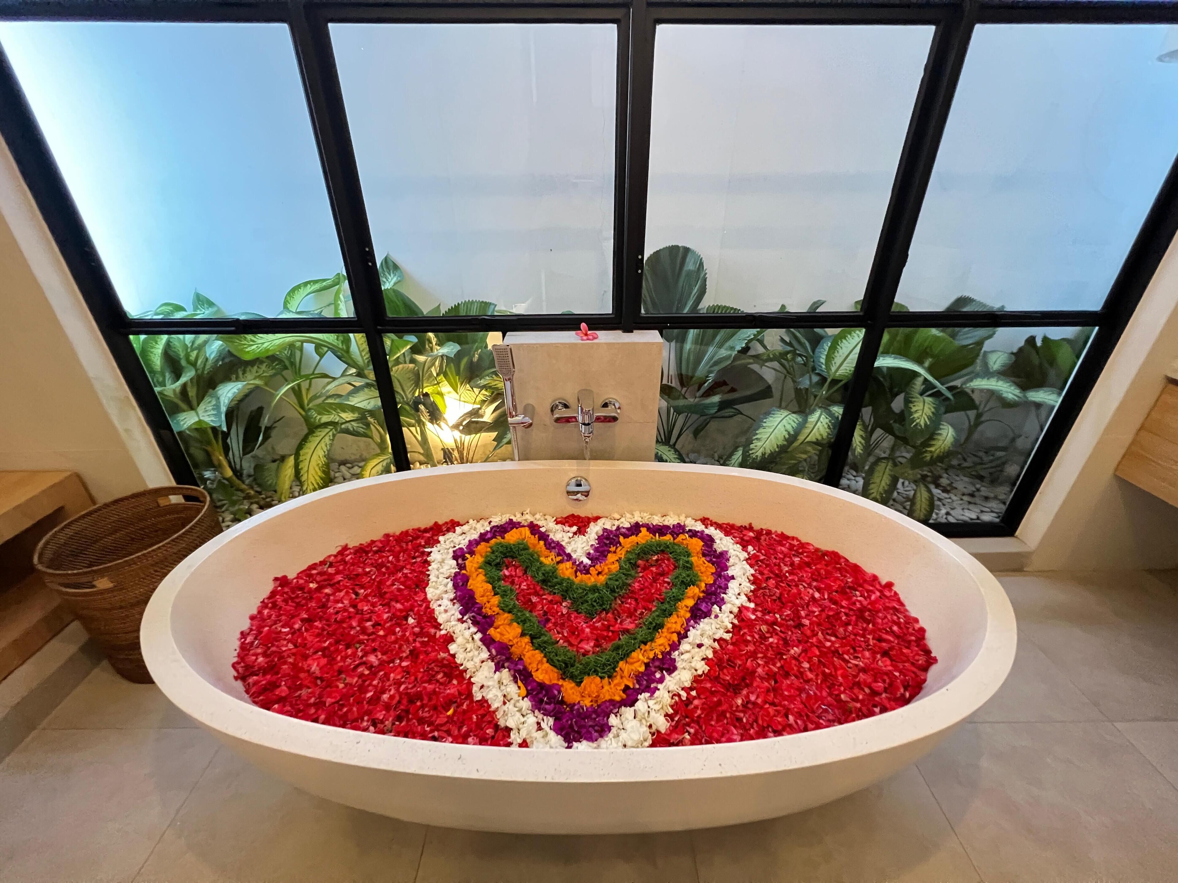 Une baignoire remplie d’eau et de pétales de fleurs disposés en forme de cœur.