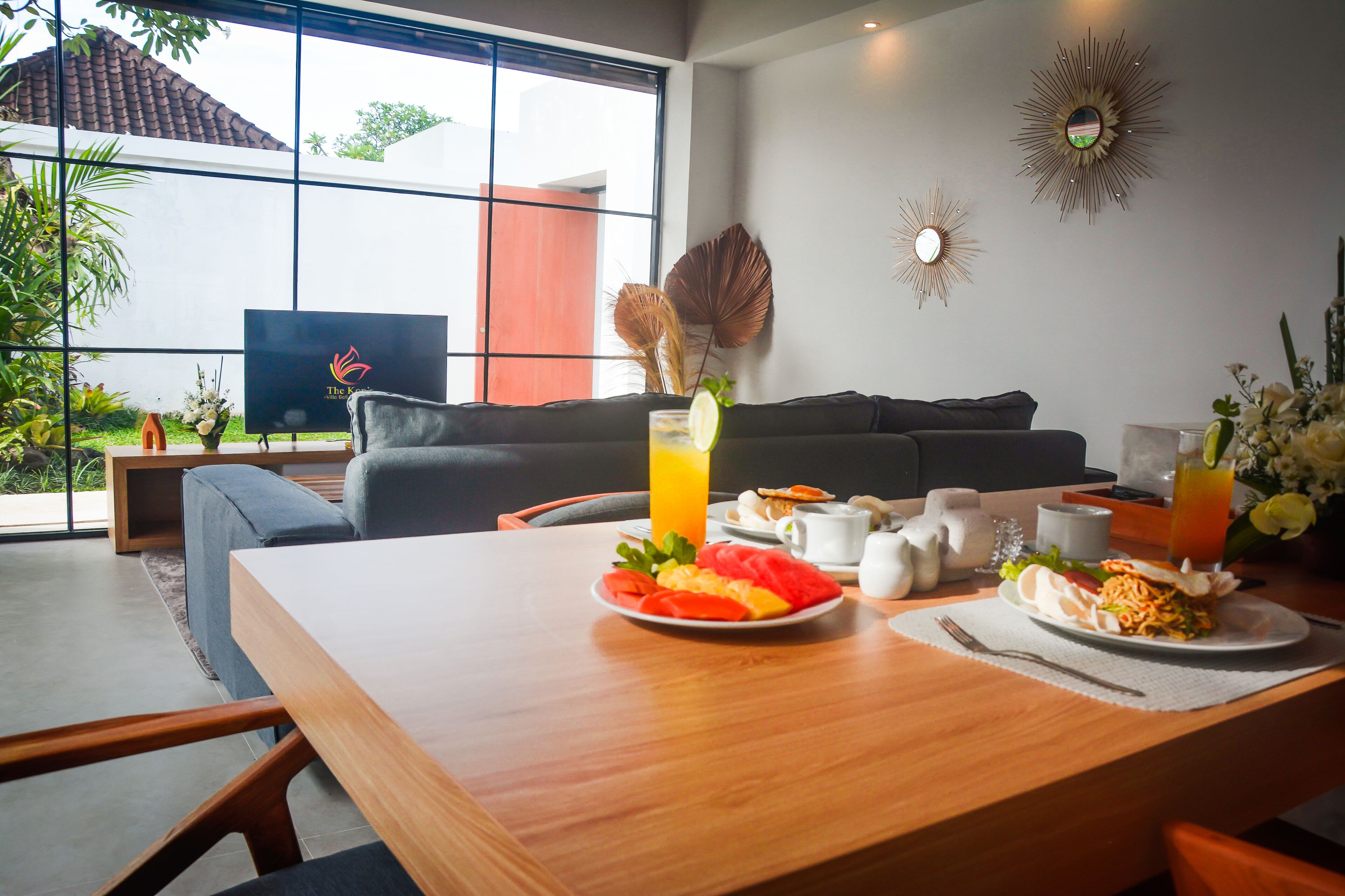 A dining area with a wooden table set for breakfast, including plates of fruit and a glass of orange juice.