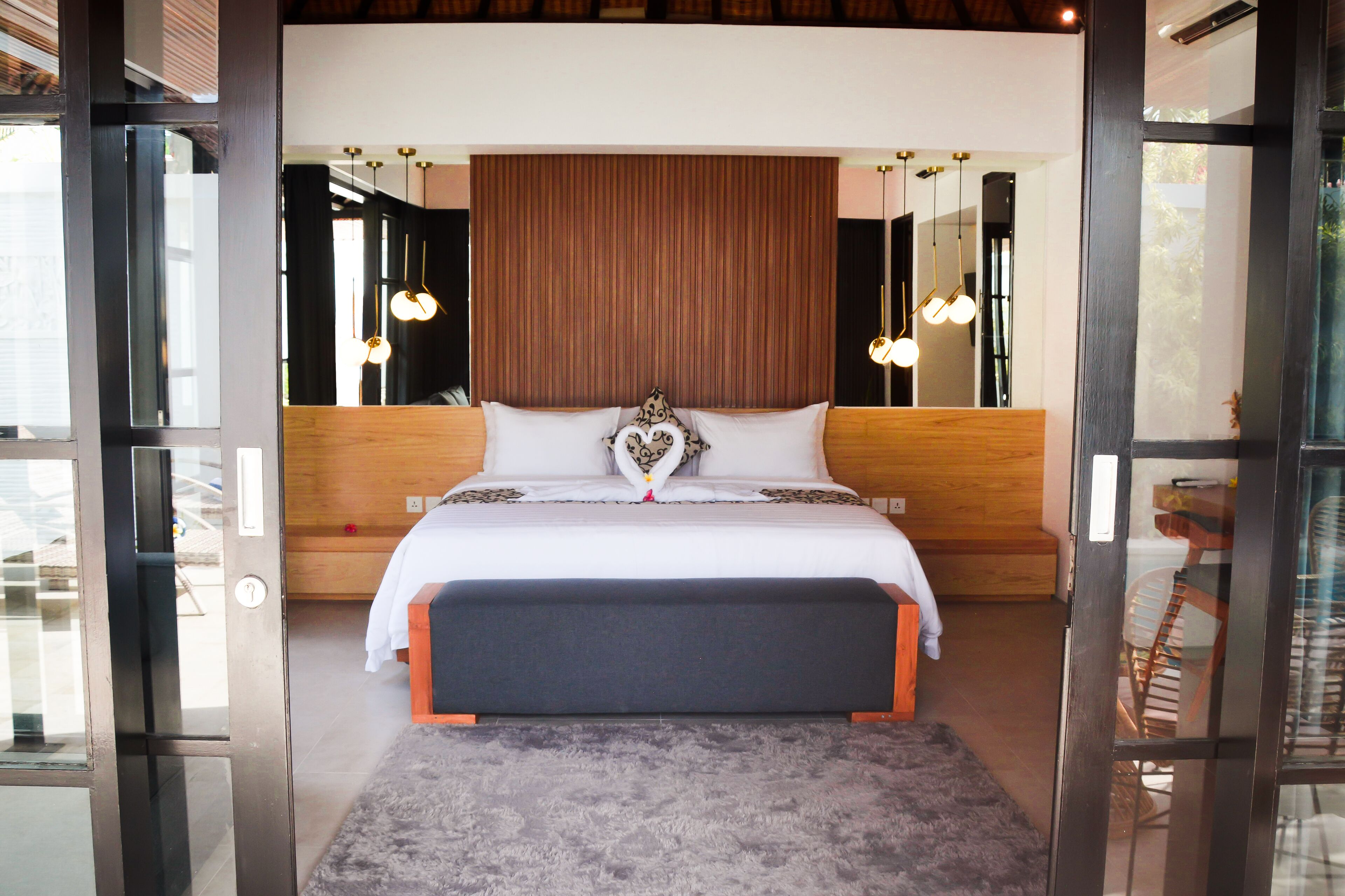 A modern bedroom with a large bed, wooden headboard, and a view through a glass door.