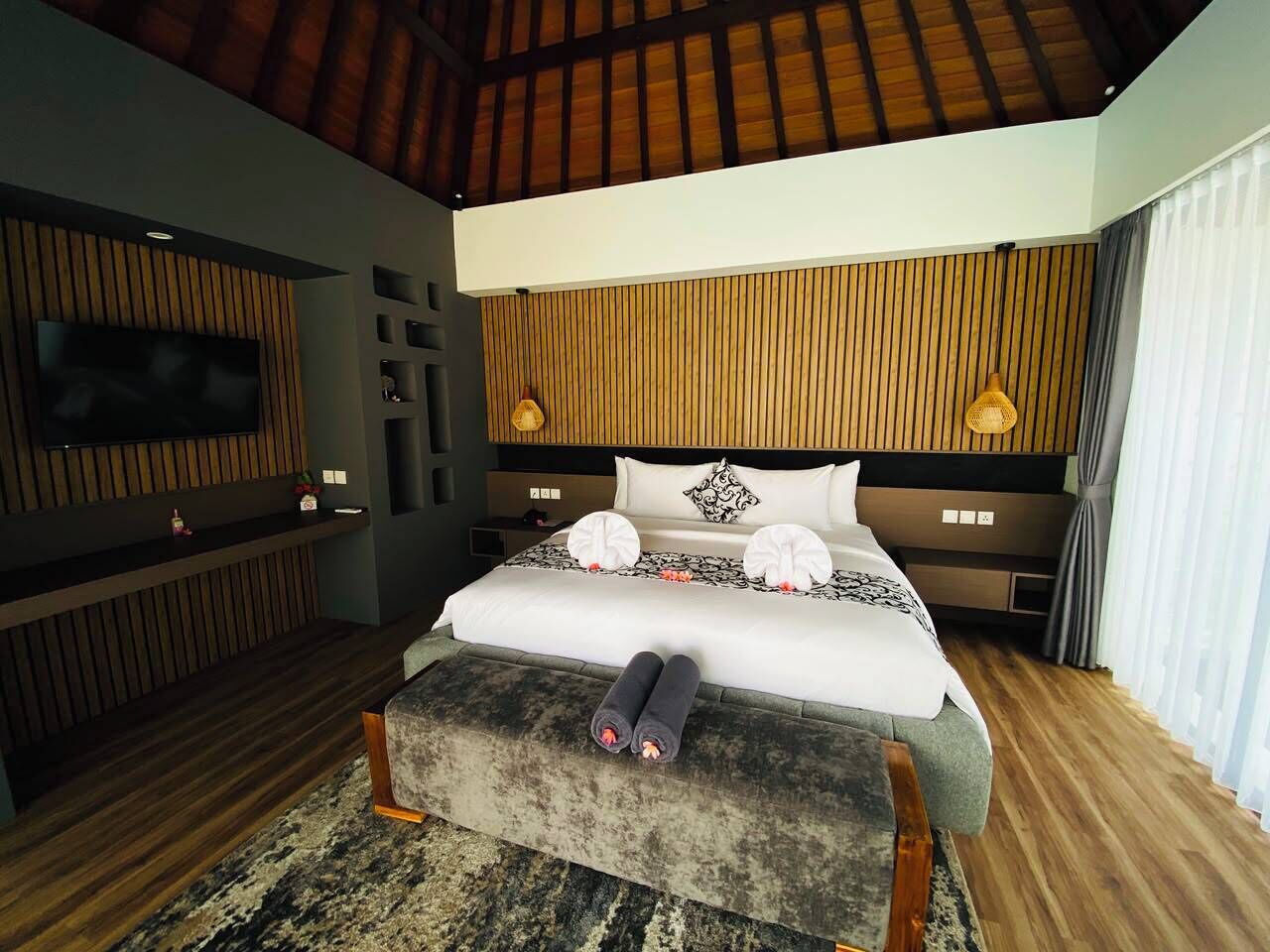 Un dormitorio moderno con una cama grande, televisión de pantalla plana, paneles de madera y techo con vigas a la vista.