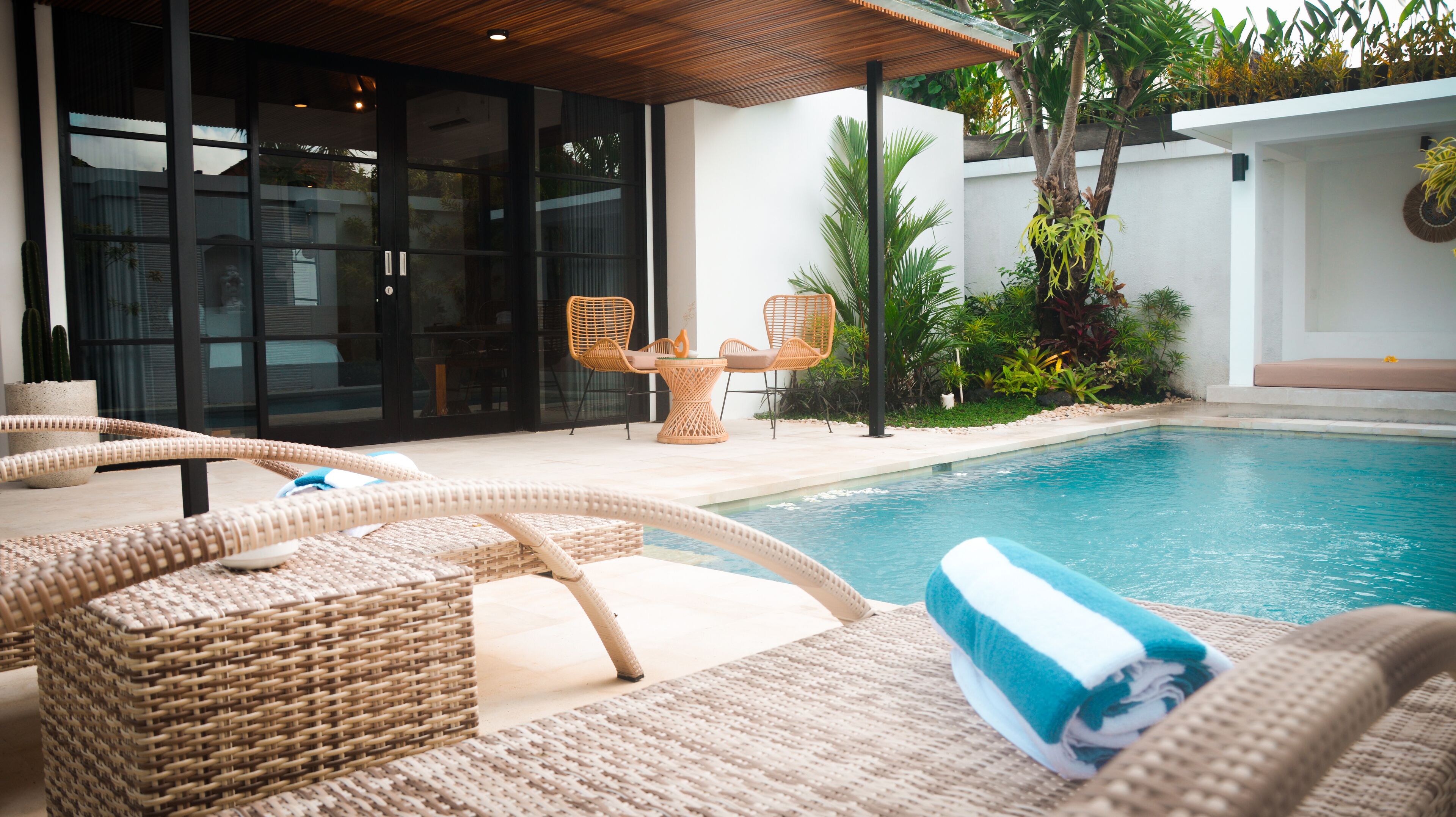A poolside area with wicker lounge chairs, a table, and a covered seating area.