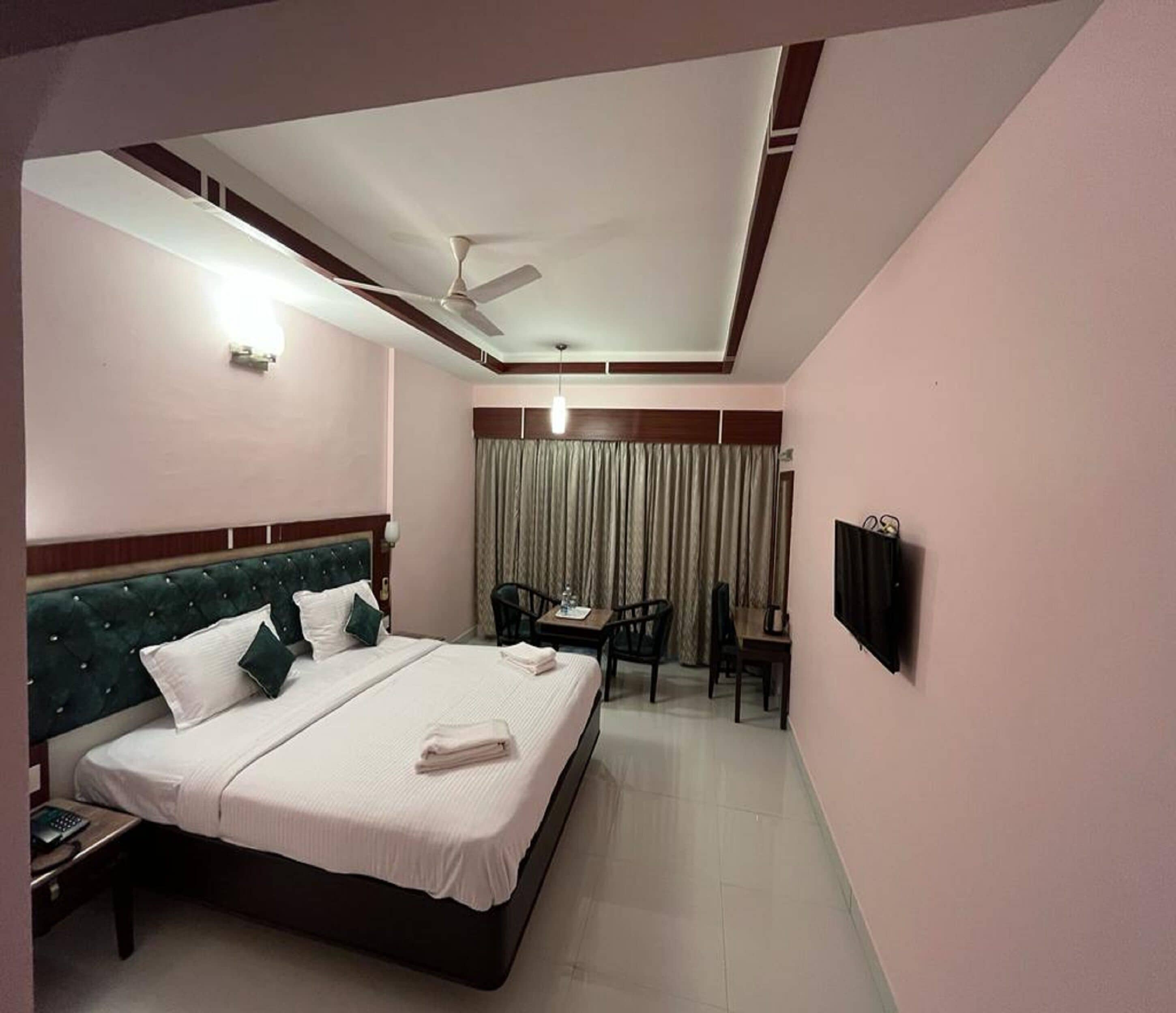 Habitación de hotel con una cama grande, un escritorio, una silla, un ventilador de techo y un televisor montado en la pared.